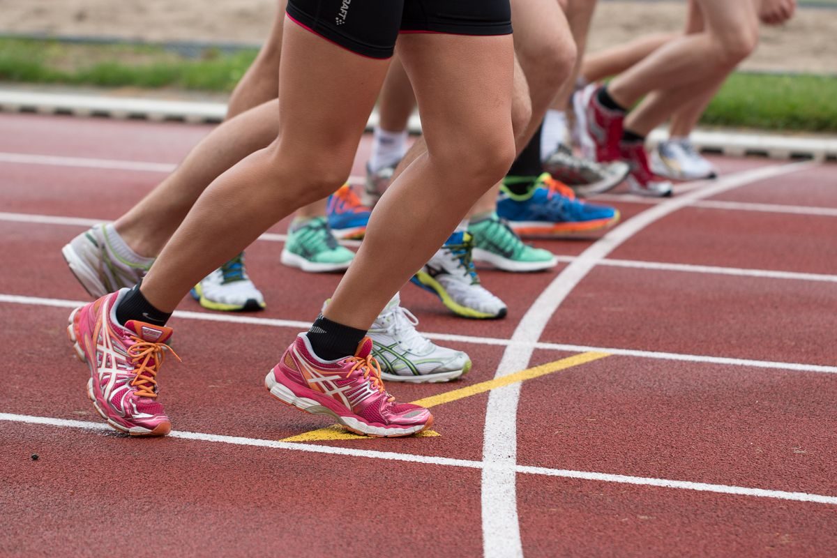 Men and women runners at the starting line of a track, photographed from the knees down